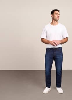 A man wearing slim fit jeans and white tee shirt is pictured on a beige backdrop.
