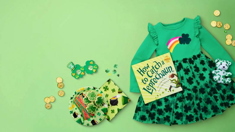 Kids green shamrock dress with rainbow detail, How to Catch a Leprechaun book, festive glasses, toy bear, cookies, candy and gold coins.