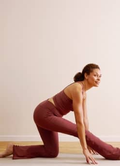 An adult in a matching workout set stretches in a low lunge yoga pose on a mat.