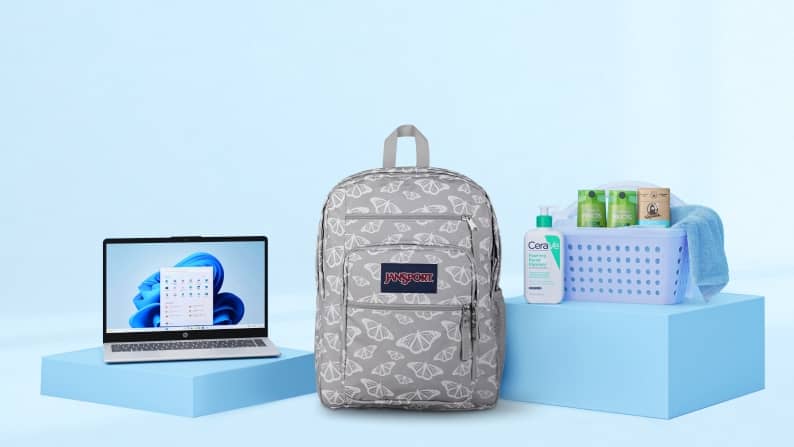 An open laptop sits on a light blue surface next to a grey patterned JanSport backpack and a plastic bin filled with personal care products.