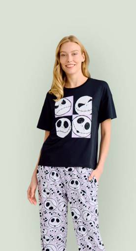 A woman wearing a Jack Skellington pajama set is pictured on a light green backdrop.