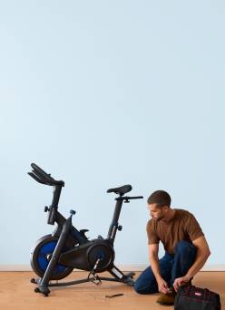 An image of a person kneeling in front of an exercise bike.