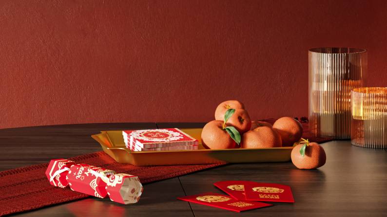 Festive tabletop scene with party cracker, red envelopes, tangerines, napkins, vase and candleholder.