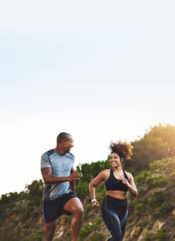 Man and woman jogging while smiling at each other in a nature setting.