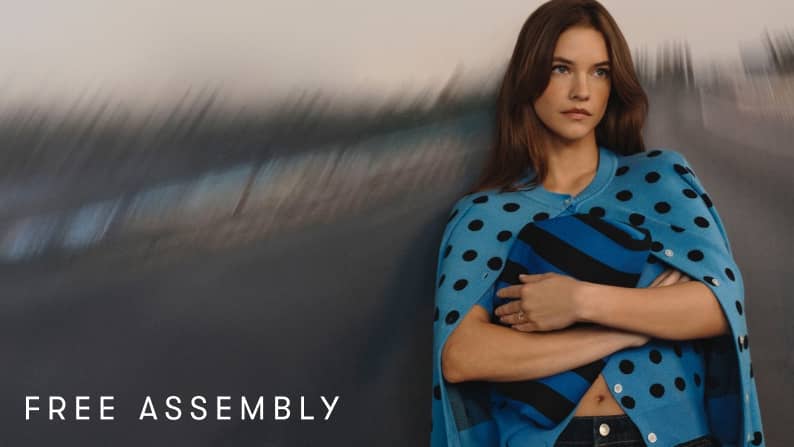 Model Barbara Palvin wears a blue polka dot cardigan over a striped top, holding a blue and black striped oversized clutch.