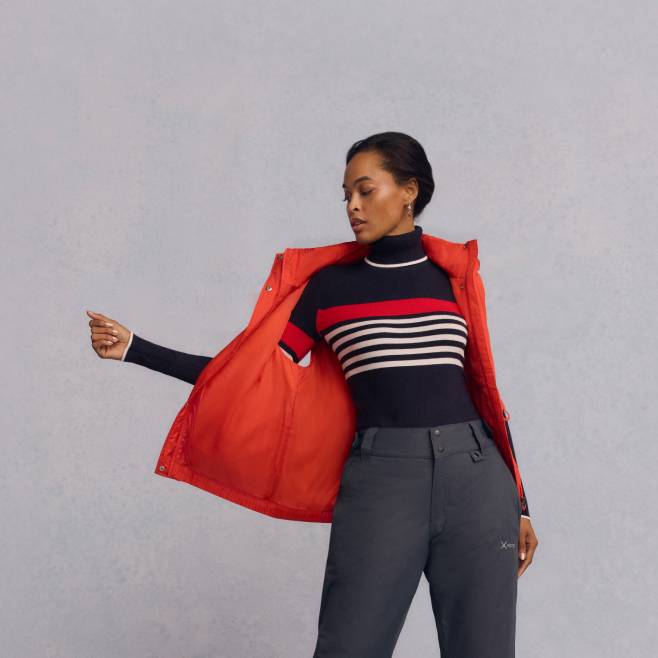 A woman is shown wearing a red puffer vest over a turtleneck sweater and snow pants.