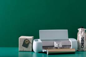 A Cricut printer surrounded by accessories and a golden roll of paper.