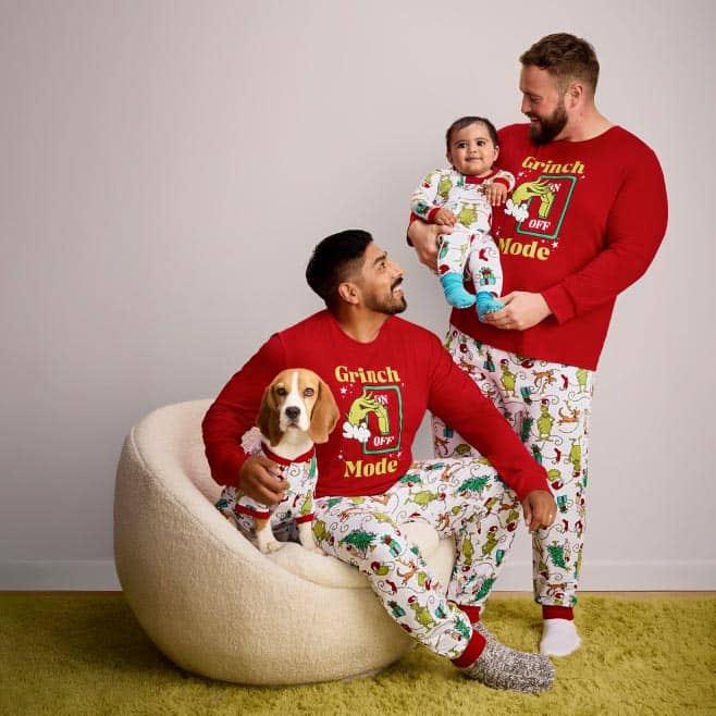 A family of three and a dog wearing matching Grinch pajamas are pictured on a beige backdrop.