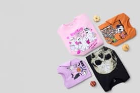 Four Halloween printed graphic tee shirts are arranged with small pumpkins.