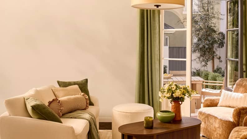 A cream sofa with green and striped pillows sits near a dark wood fluted coffee table styled with flowers, a candle and green decorative bowls.