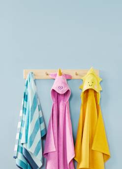 Three towels hang on a wooden rack: one blue striped, one pink unicorn, and one yellow sun. Reads: Bathtime joy. Fresh finds from seven eighty-three.