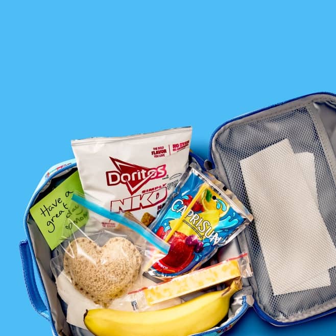 A lunchbox with Doritos NKD, a banana, a Capri Sun, a colby-Jack cheese stick, and a heart-shaped sandwich.