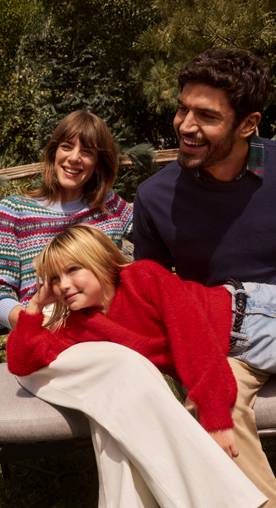 A family of four is shown sitting outside on a bench. Everyone is wearing sweaters.