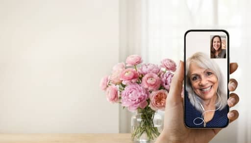 A vase on a tableand a and holding a phone with a picture of two people on a video call.