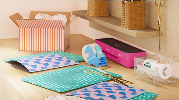 Colorful mailers and boxes on a wood table next to tape, scissors and a printer.
