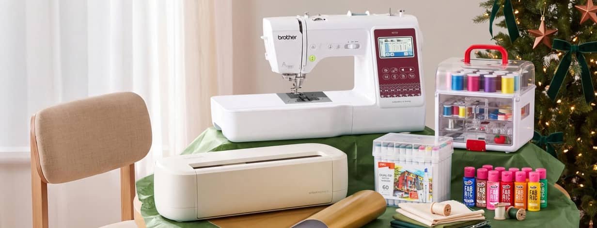Brother sewing machine with cutting machine, thread case, markers and fabric paints on a table for holiday crafts.