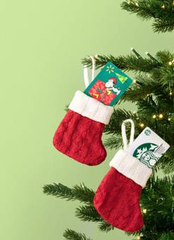 An image of Snoopy and Starbucks gift cards in Christmas stocking ornaments, hanging on a tree with white lights.