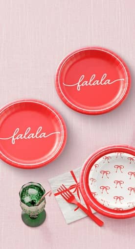 Image shows red and white holiday tableware with red cutlery, red napkins, and green glasses.