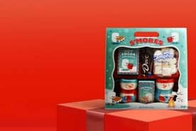 A Dove chocolate s’mores mug gift set with cocoa mix and candy on a red gift box against a red background.