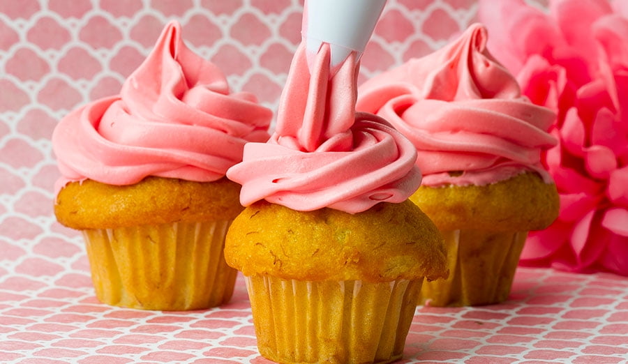 3 cupcakes being decorated with pink icing