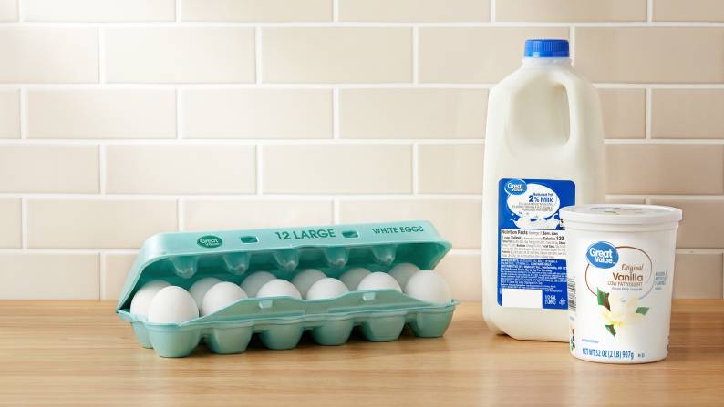 A dozen Great Value eggs, half a gallon of Great Value two percent milk, and Great Value vanilla low-fat yogurt on a counter.
