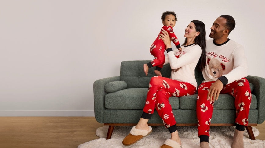A family of three wearing matching bear pajamas are pictured sitting on green couch.