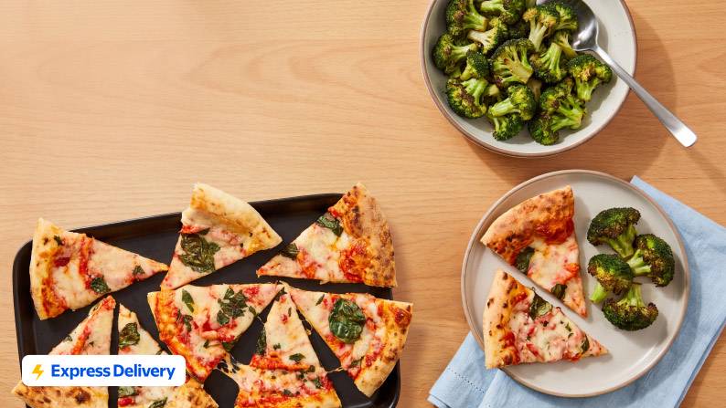 Sliced pizza and broccoli on plates and bowls on a wood tabletop.