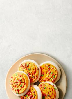 A plate of sugar cookies with orange icing and fall-themed sprinkles is shown.