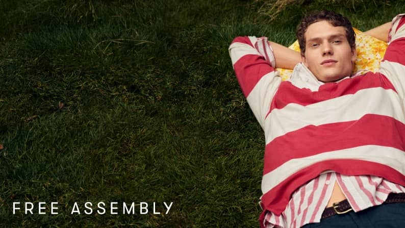 A man in jeans and a red-and-white rugby shirt over a red-and-white button-up, laying down on the grass.