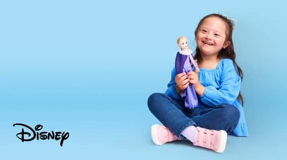 Image of a girl holding a Disney Frozen Elsa doll with a purple dress on a blue background. The Disney logo is shown.