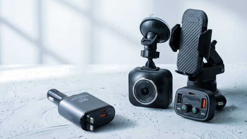 Car dash camera, phone mount and dual port car chargers arranged on a light textured surface.