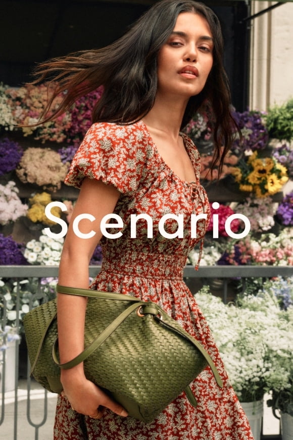 Woman in front of a flower stand wearing a floral puff-sleeve smocked dress with an olive-green tote.