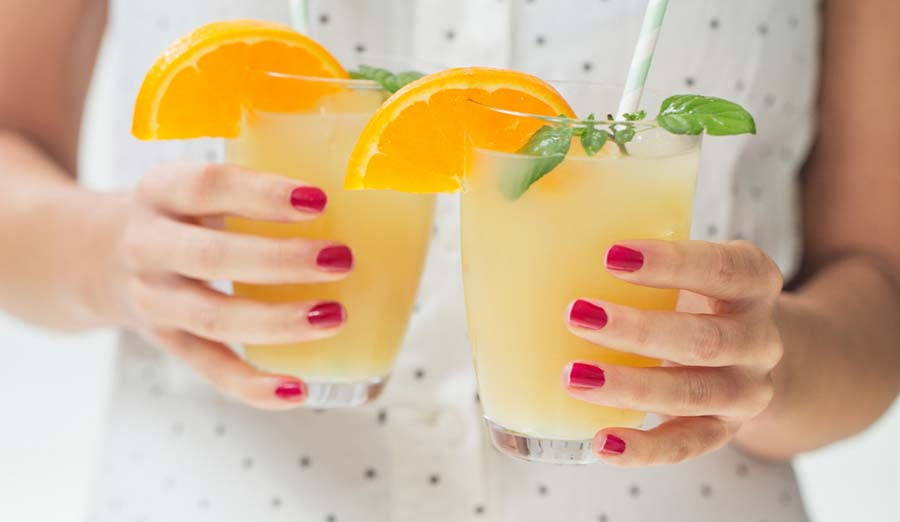 woman holding two orange drinks in glasses
