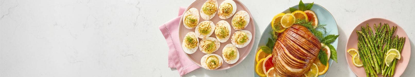 A plated spread is shown with baked ham, deviled eggs, green beans and carrots.