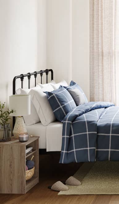 A bedroom scene complete with a bed frame, mattress, blankets, side table & slippers tucked under the bed.