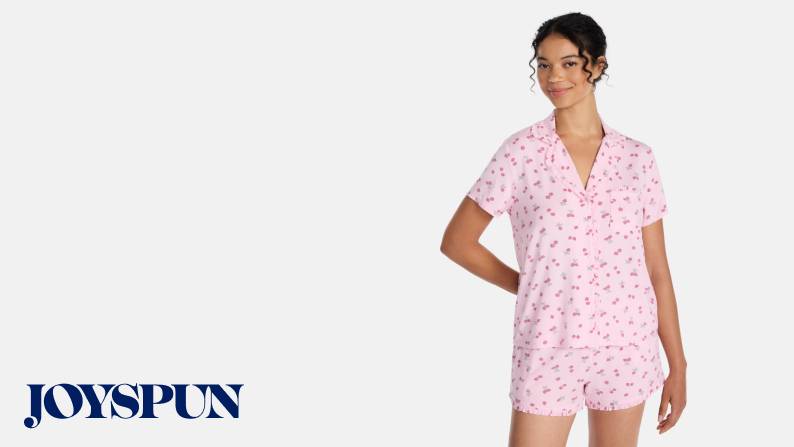 Woman posing in a pink cherry-print short-sleeve pajama shirt and matching shorts.