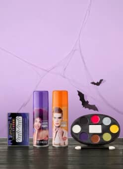 Makeup including false eyelashes, two cans of colored hair spray, makeup palette and applicator. The background is decorated with bats and webs.
