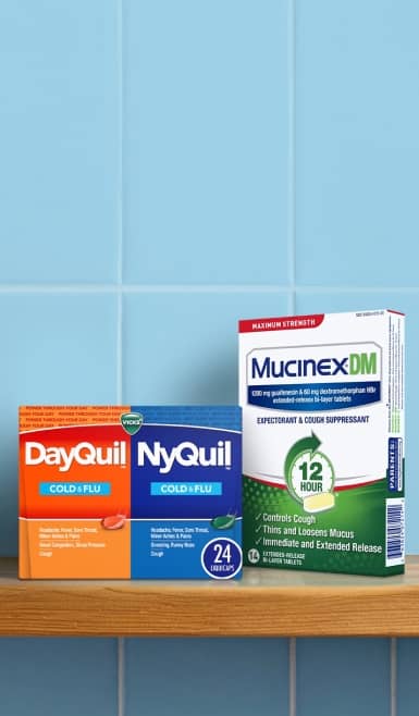 Packages of Dayquil, Nyquil and Mucinex on a wood shelf with a blue subway tile background.