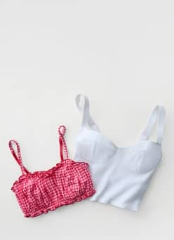 A red checkered gingham ruched bra and a white ribbed corset bra are pictured.