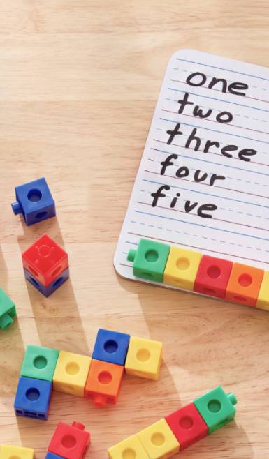 Colorful interlocking blocks on a wooden surface next to a notepad with numbers spelled one, two, three, four, five.