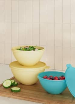 Stacked food storage bowls with lids on a kitchen counter, filled with salad and berries.