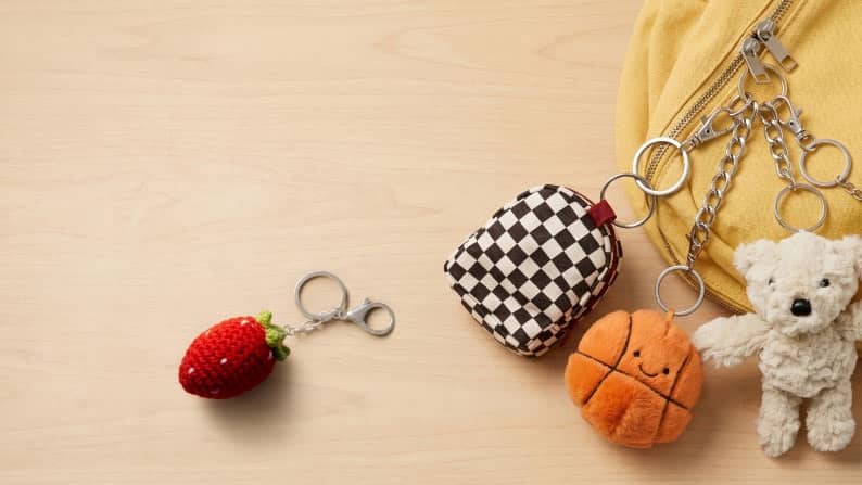 Bear, backpack, strawberry and basketball bag charms next to a yellow bag on a wood table.