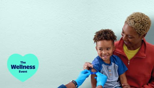 The Wellness Event. A child sits on a woman’s lap while a healthcare professional applies a band aid to the child’s arm.