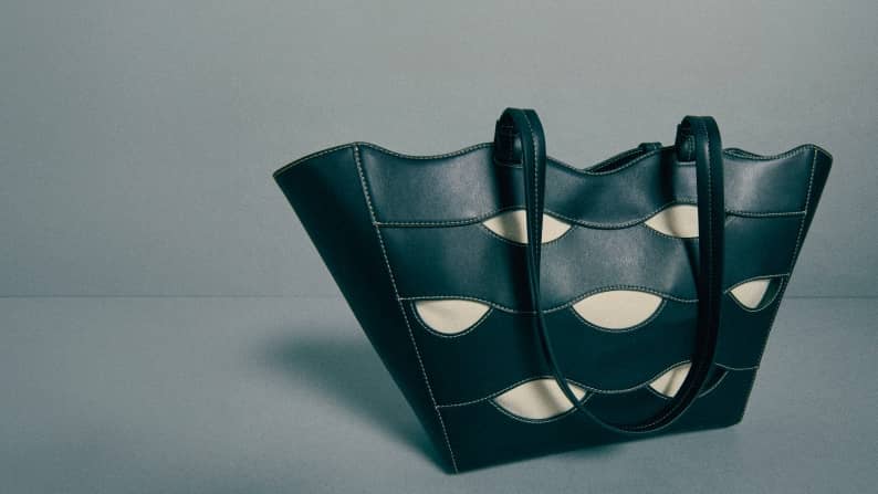 Black tote bag with light beige cutouts and curved details against a gray background.