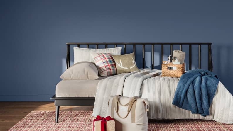 A day bed with throw pillows, bath accessories and weekender bag rest on a rug in slate blue room.
