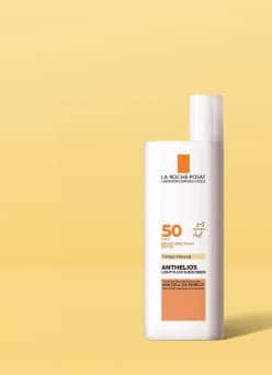 A bottle of La Roche-Posay Anthelios Tinted Mineral SPF 50 sunscreen with a white and orange label against a yellow background.