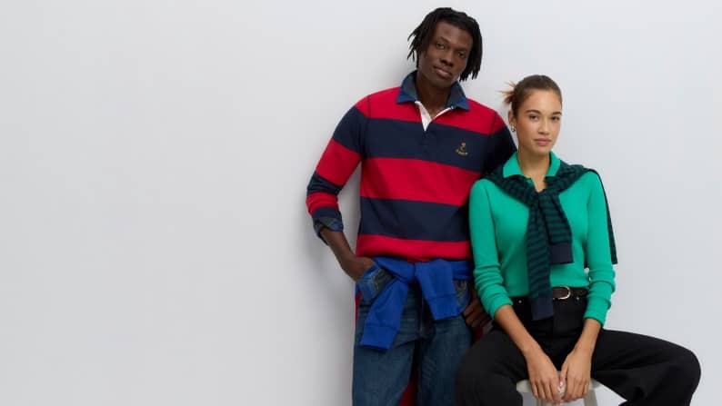 Two adults in casual striped rugby and bright sweater outfits pose together against a plain background.