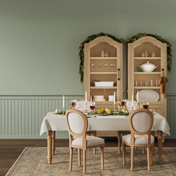 A sage green dining room features two hutches and a dining table set adorned with tableware and decor.