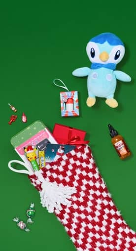 A red and white checkered Christmas stocking is full of goodies and is surrounded by candy, a stuffed toy and more.