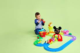 Image of a boy playing with a Fisher-Price Disney Mickey Mouse Clubhouse Train Set on a light green background. The Disney logo is shown.